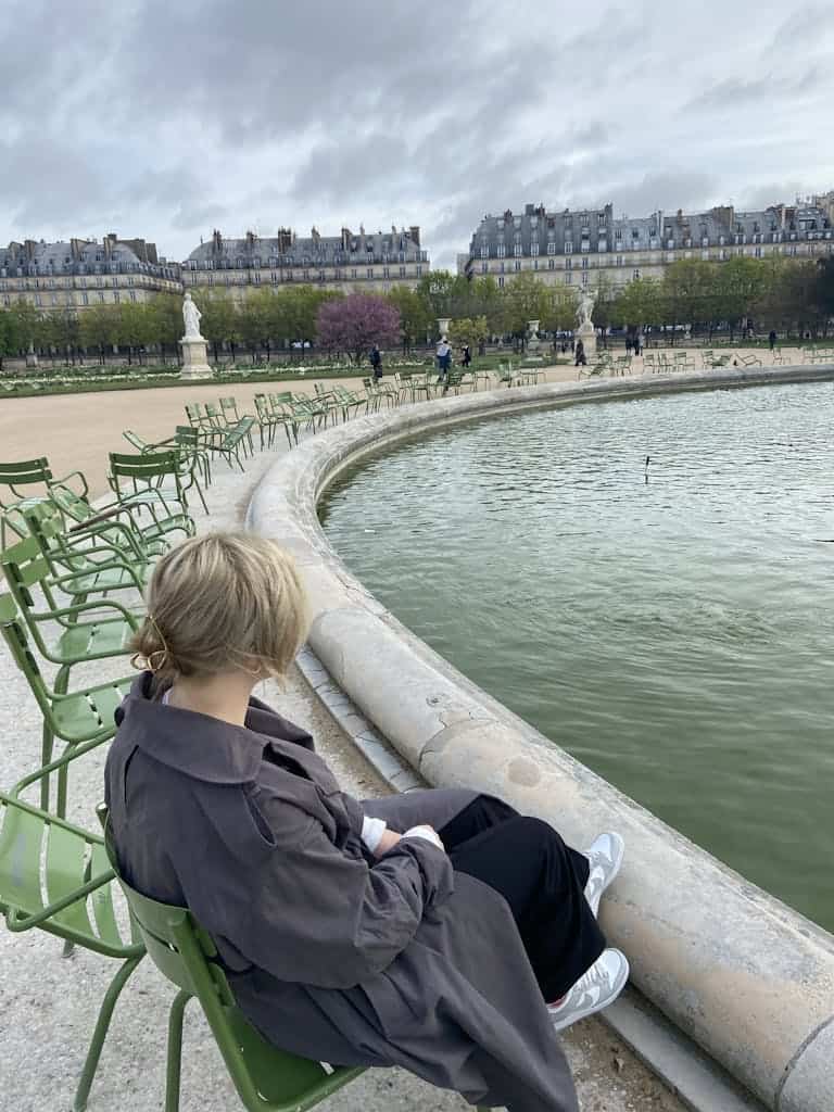 A woman sitting in Tuileries Garden enjoying a peaceful morning by the fountain in Paris.