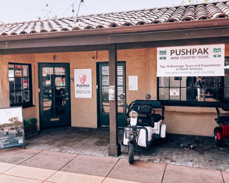 Outdoor view of Pushpak Motors entrance with signage for wine tours and transportation services. Bike accessible with welcoming storefront for wine tasting and beverage experiences.