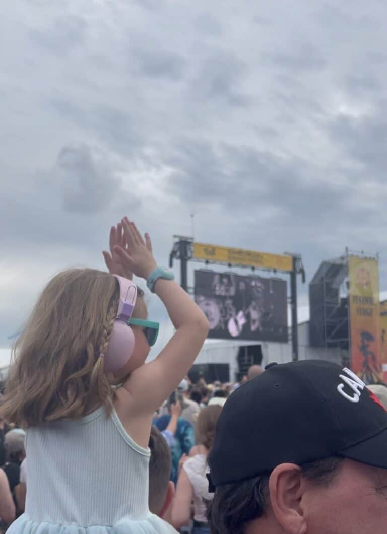 young girl with pink headphones dancing at outdoor music festival.